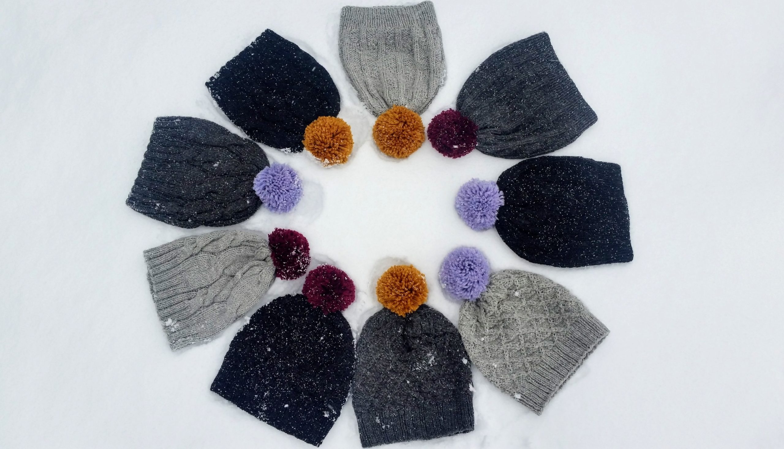 A collection of grey knit hats with colourful pompoms that are arranged in a circle in the snow