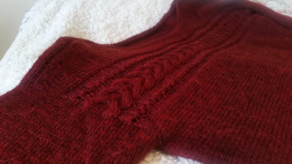 A close up of a cable running horizontally across the chest of a red knit pullover.