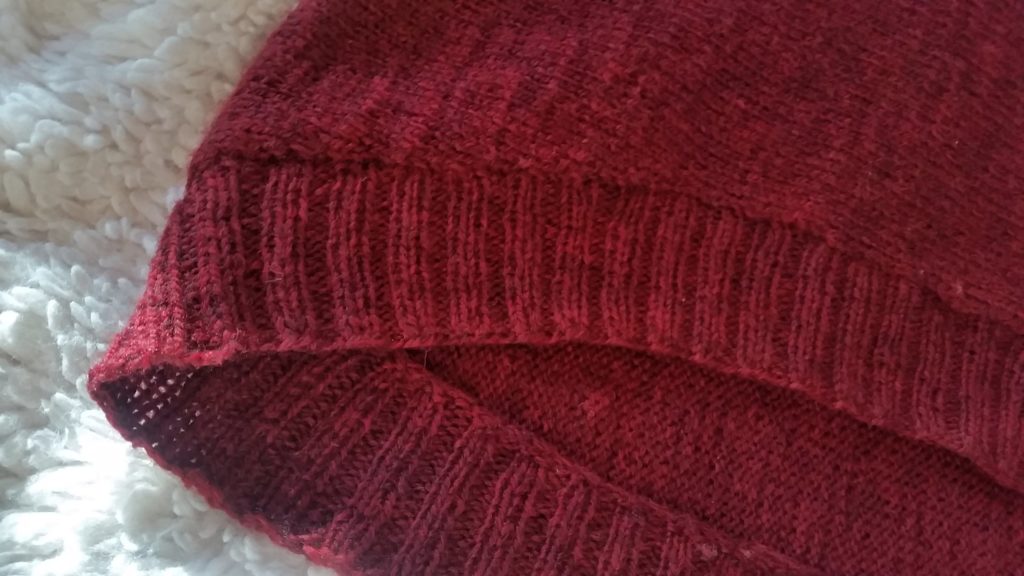 A close up of the ribbing at the bottom of a red knit pullover