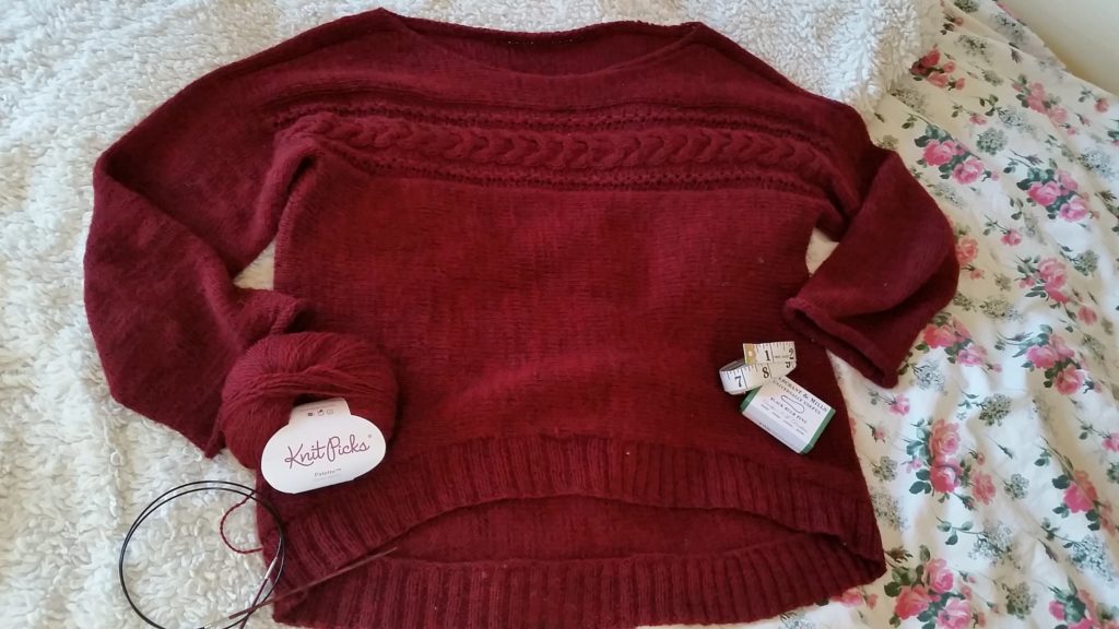 A red knit pullover is laid flat on a floral bedspread with a fuzzy blanket behind.